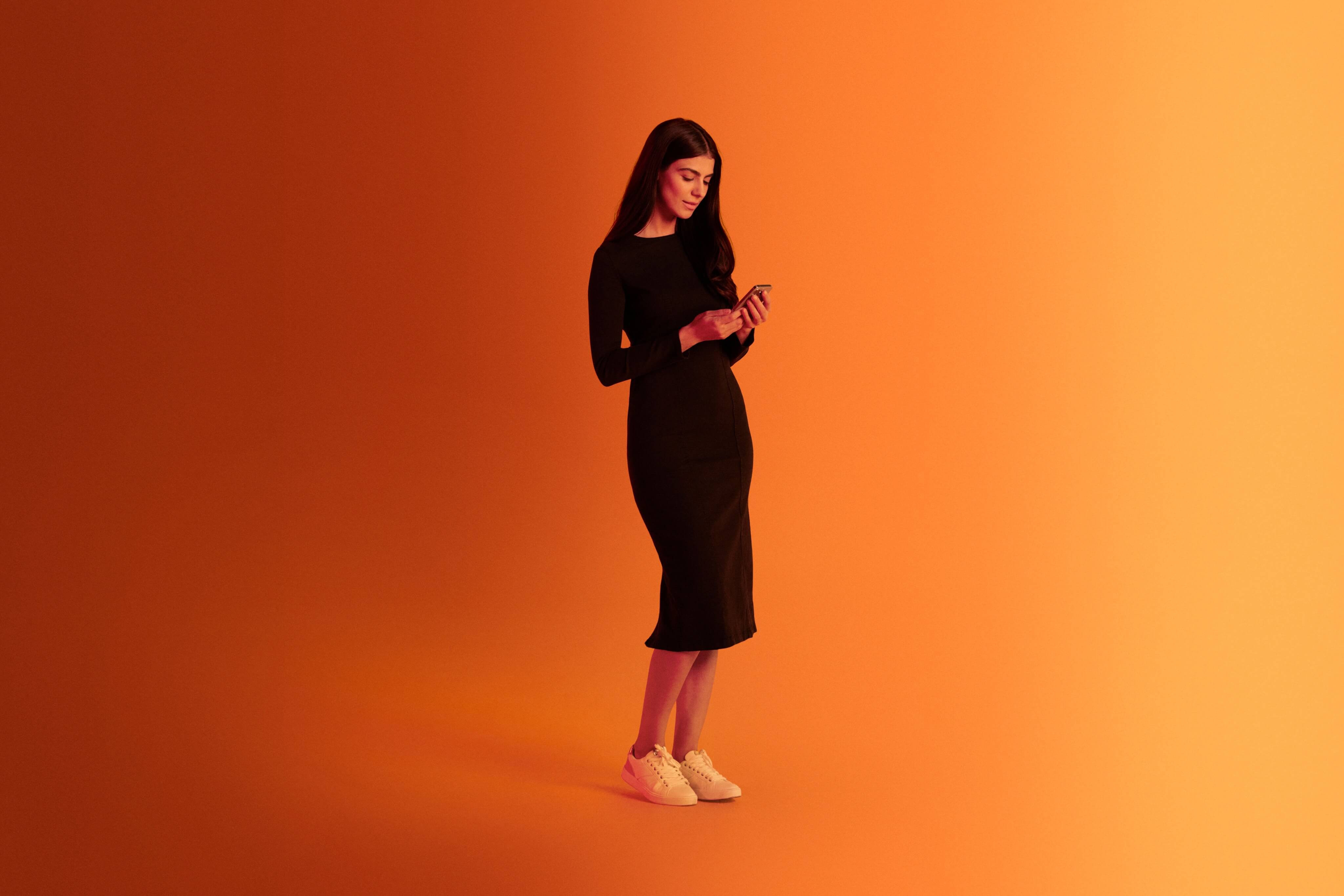 tanding woman engaging with the Xapo Bank app on her mobile phone, overlaid with an orange hue.
