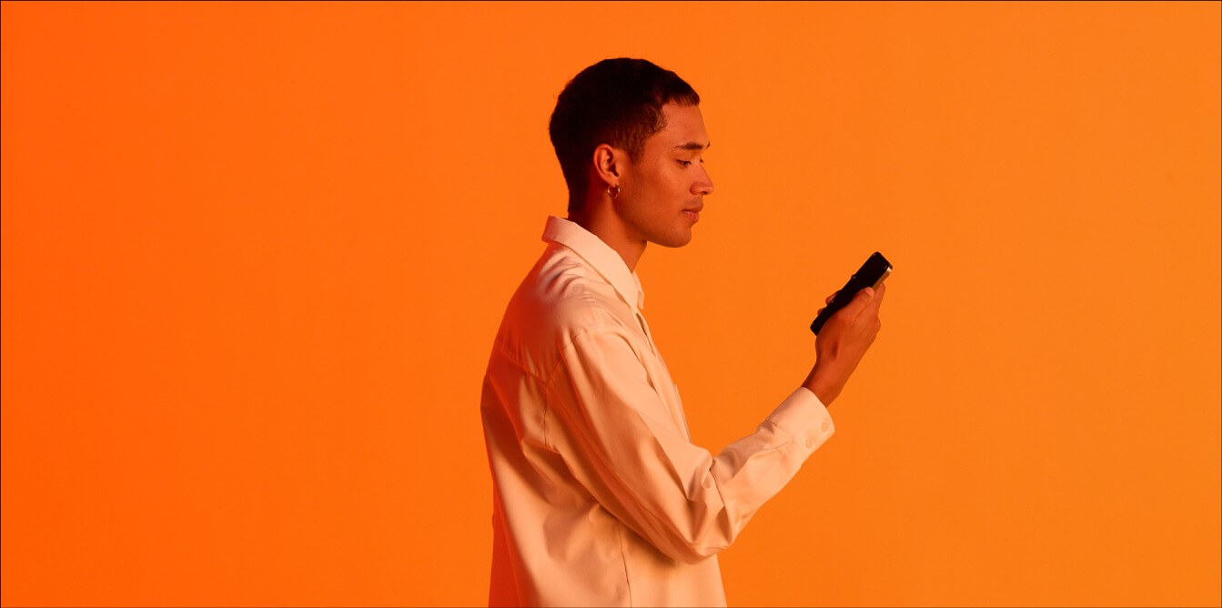 Man engaging with his mobile phone against an orange background.
